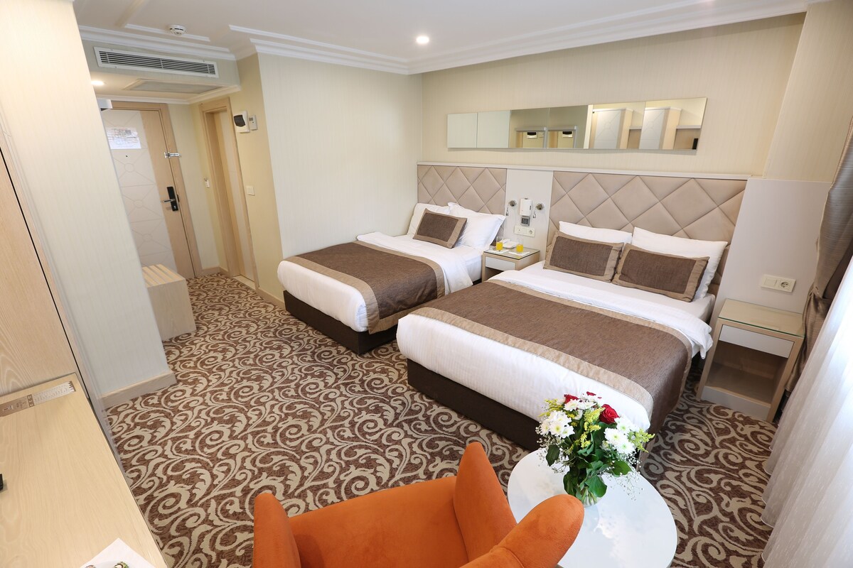 A hotel room with two beds, a small table with a vase of flowers, and a chair.