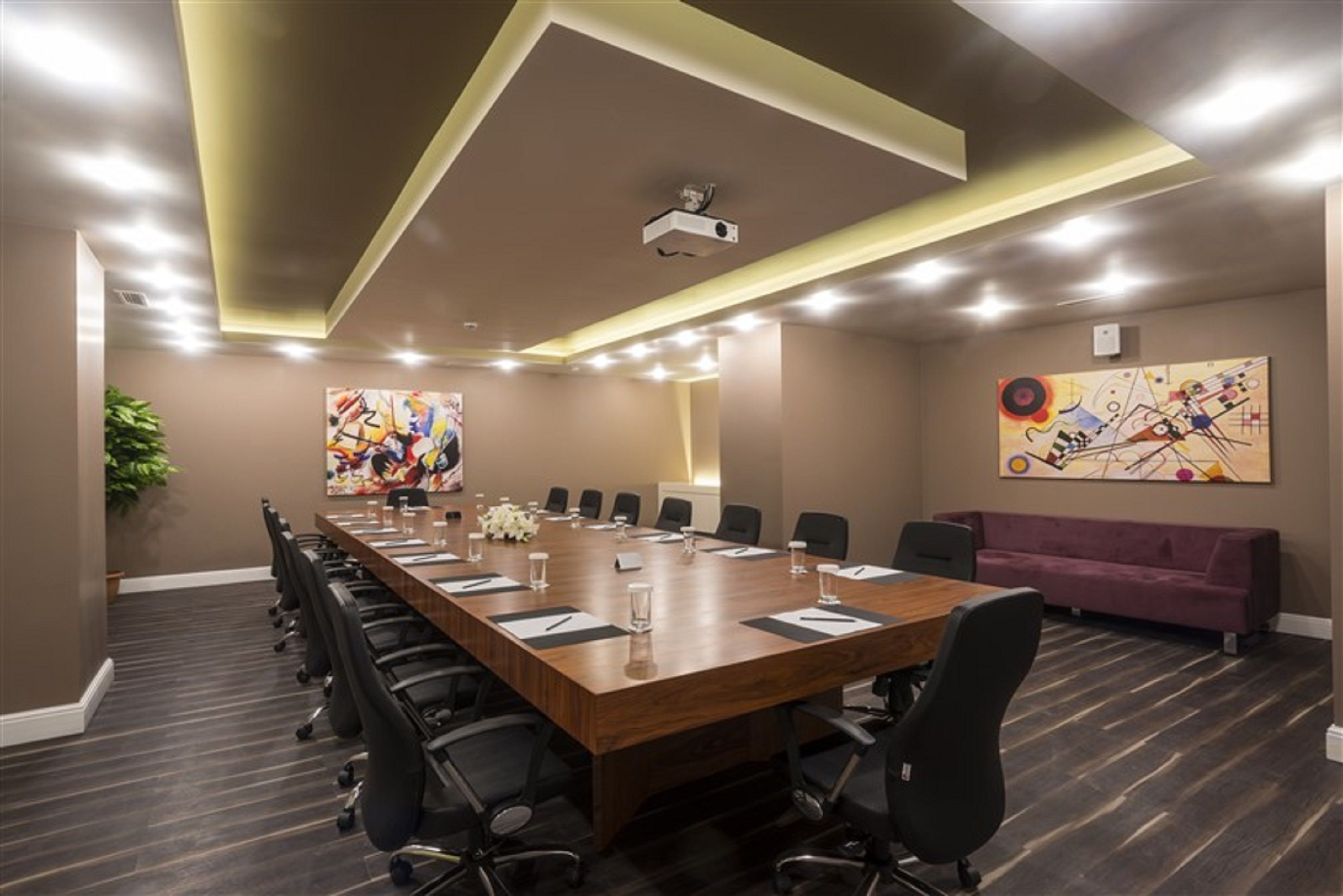 A conference room with a long table, chairs, a projector, and artwork on the walls.