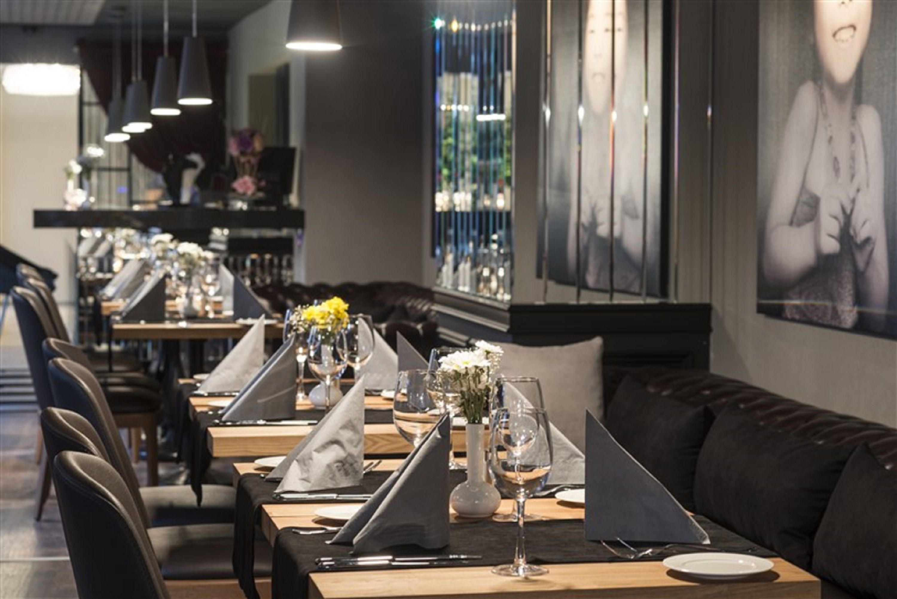 Een restaurant met lange tafels gedekt voor een maaltijd, met zwarte leren zitjes en een bar op de achtergrond.