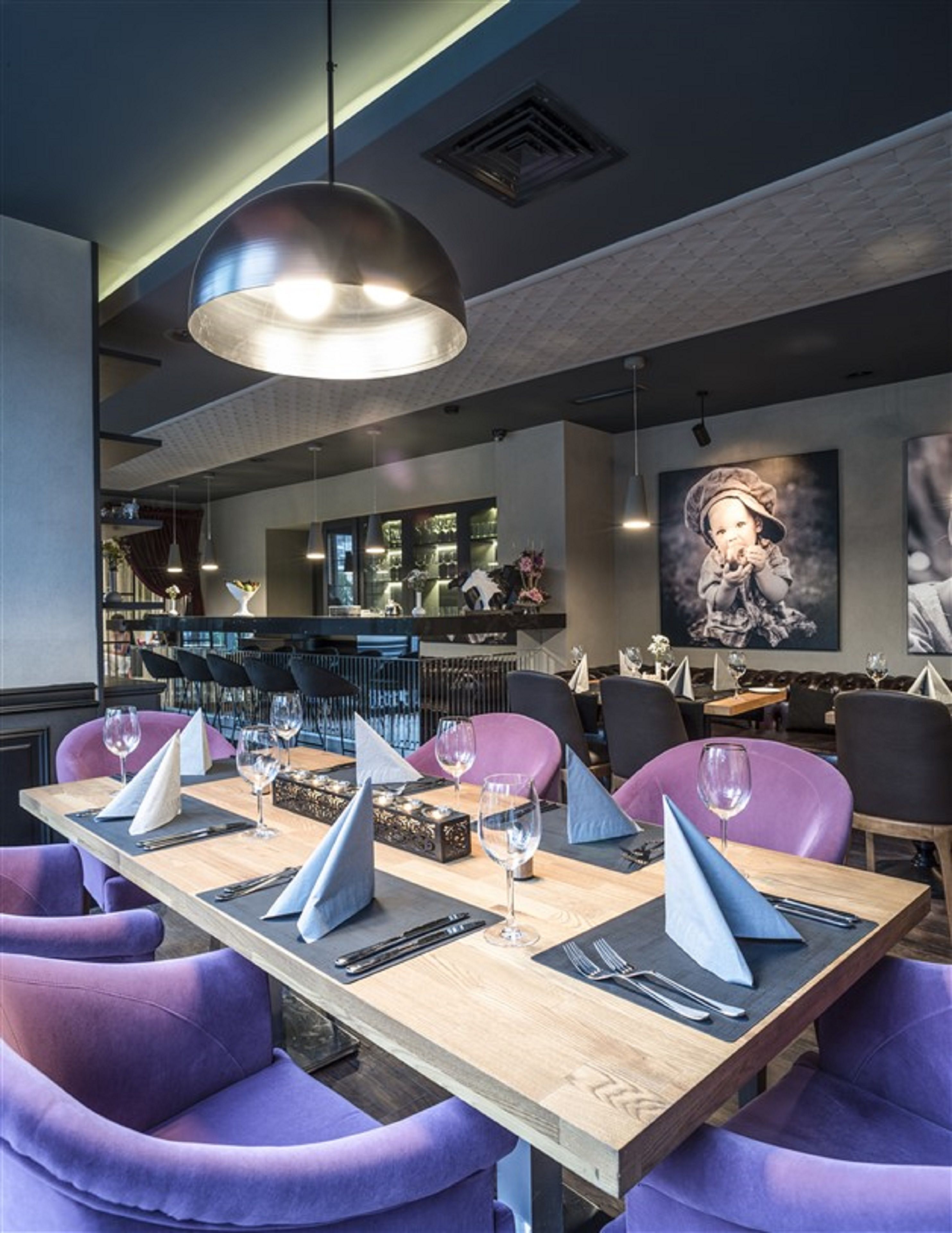 Un restaurante con una larga mesa de madera dispuesta para comer, sillas tapizadas de color púrpura y una lámpara colgante grande.