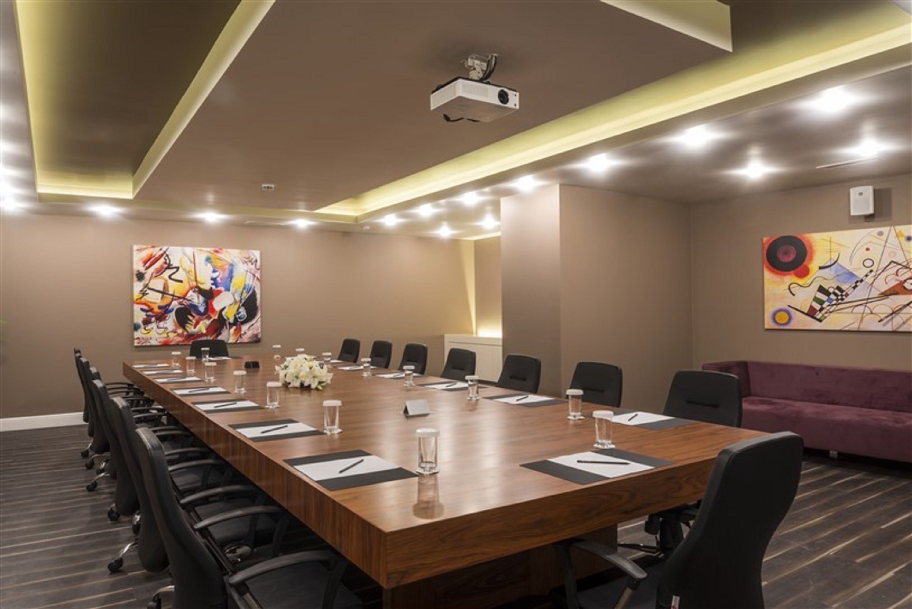 A conference room with a long wooden table, black chairs, and a projector on the ceiling.
