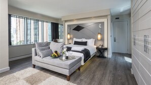 Une chambre d’hôtel moderne avec un grand lit, un canapé et une table à manger. On y trouve une fenêtre avec des rideaux, un luminaire fixé au mur et une porte.