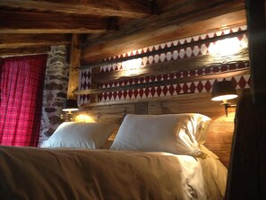 Una cama con sábanas blancas en una habitación rústica con vigas de madera y un papel tapiz estampado.
