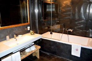 Un baño moderno con un espejo grande, dos lavamanos, una bañera y un banco.