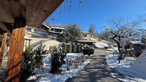 Un sentier enneigé mène à un bâtiment doté de nombreux balcons, et on aperçoit un télésiège au loin.