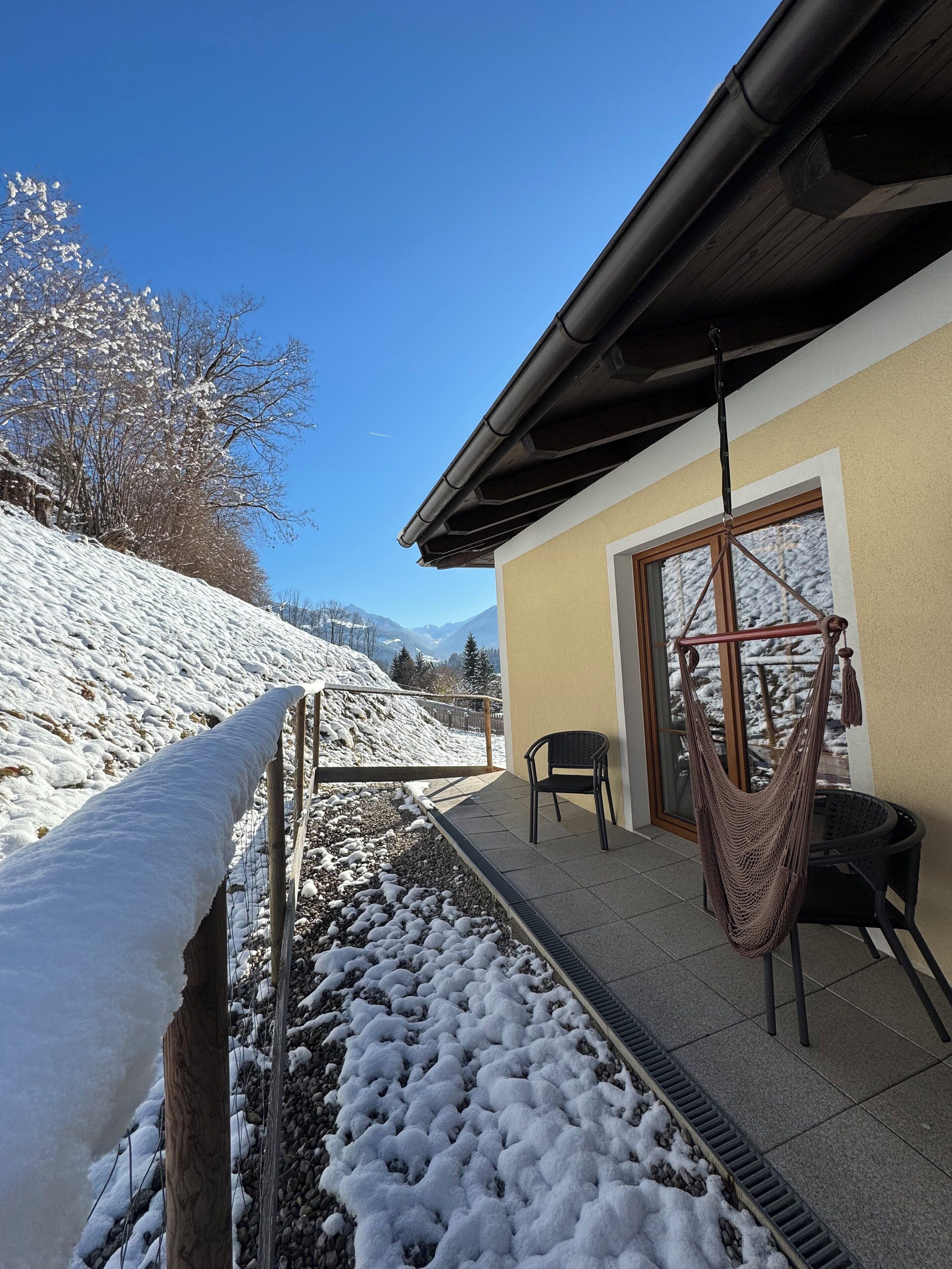 A snow-covered outdoor area with a patio, a hammock, and a view of mountains.