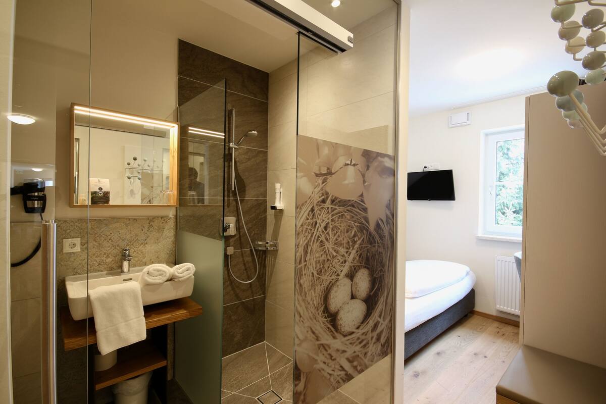 Une salle de bain moderne avec une douche à parois de verre, un lavabo avec une serviette et un téléviseur fixé au mur.