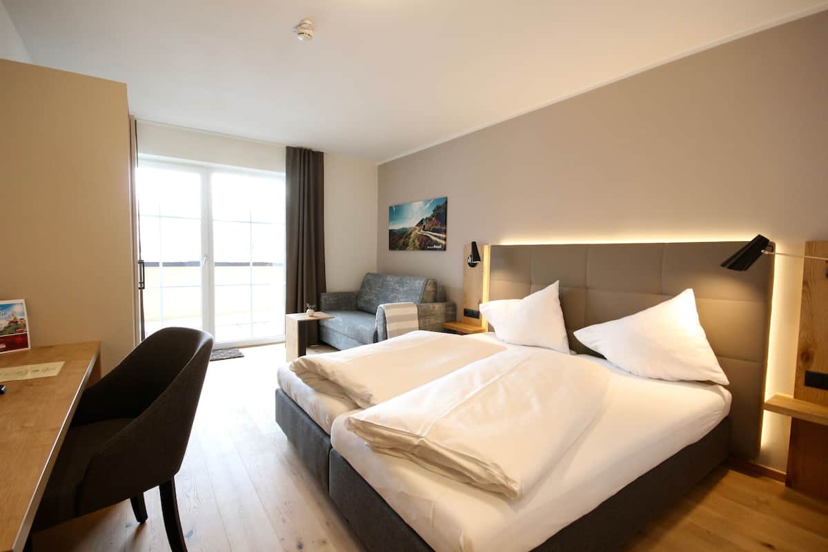 Une chambre d’hôtel avec un grand lit, un bureau, une chaise, un canapé et une fenêtre avec des rideaux.