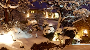 Un paysage enneigé avec un bâtiment en pierre et une fenêtre illuminée, évoquant une atmosphère chaleureuse et hivernale.