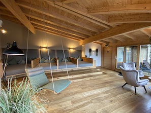 Un interior moderno con techo de madera, un sofá con cojines, una silla y una lámpara colgante.