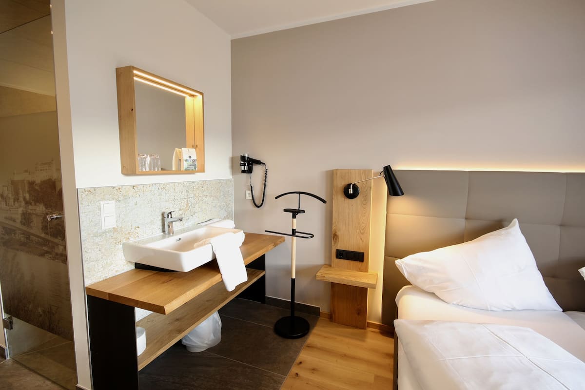 Une chambre d’hôtel moderne avec une coiffeuse en bois, un grand miroir, une table de chevet, une lampe noire et un lit avec une literie blanche.