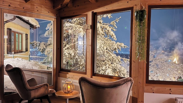 Une pièce chaleureuse avec des poutres en bois, de grandes fenêtres donnant sur un paysage enneigé et des sièges confortables.