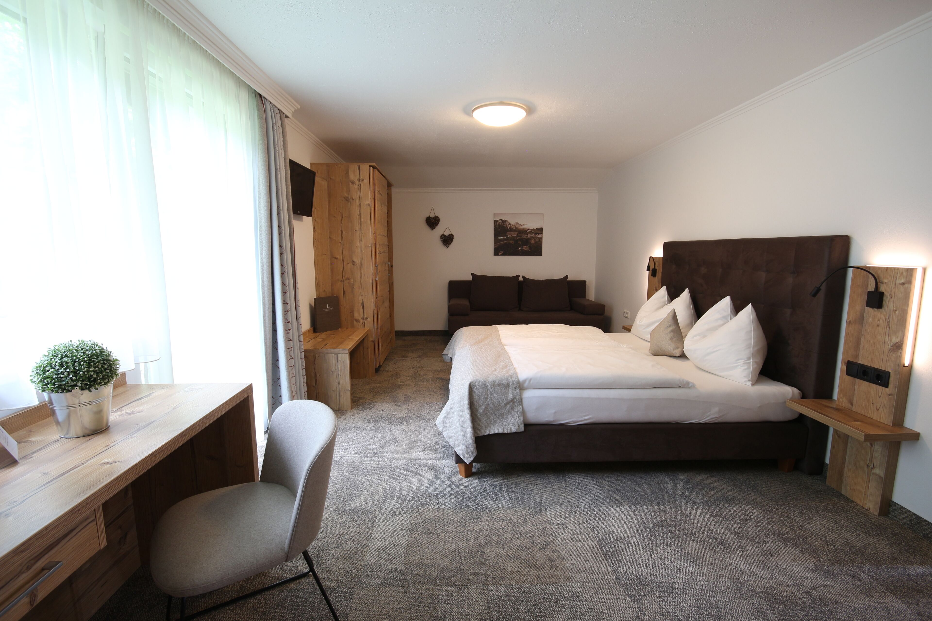 A hotel room with a bed, desk, chair, and a small potted plant.