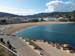 Un pueblo costero con una playa de arena, un paseo marítimo y edificios al fondo.