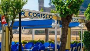 Un restaurante llamado "R CORISCO" con terraza y vistas a un edificio histórico.