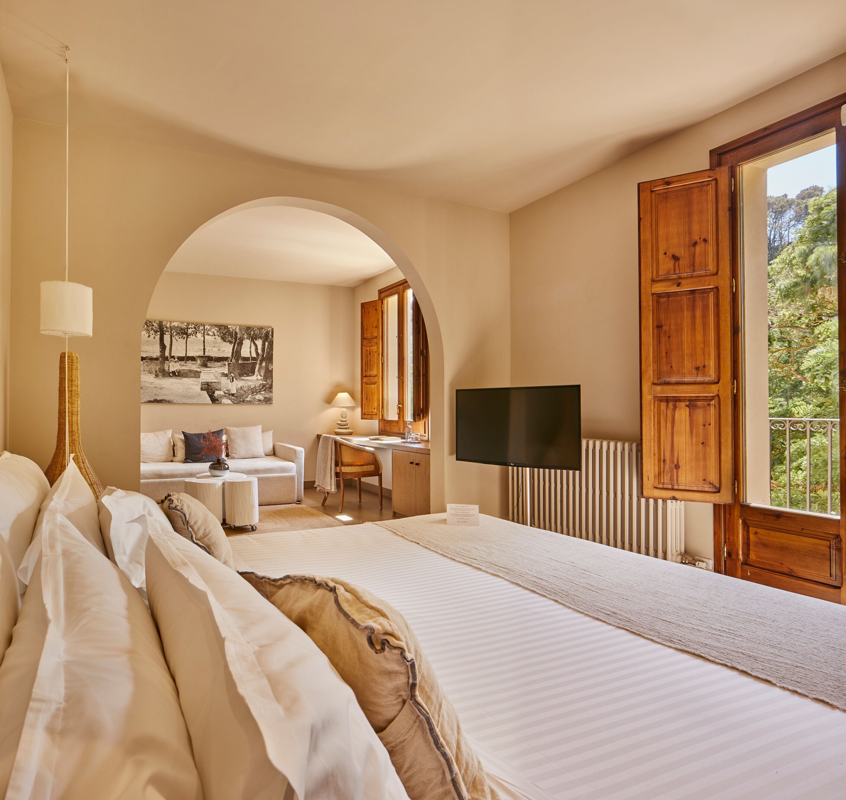 Un dormitorio con una cama grande, un escritorio, una silla, un televisor y un arco que da a otra habitación.