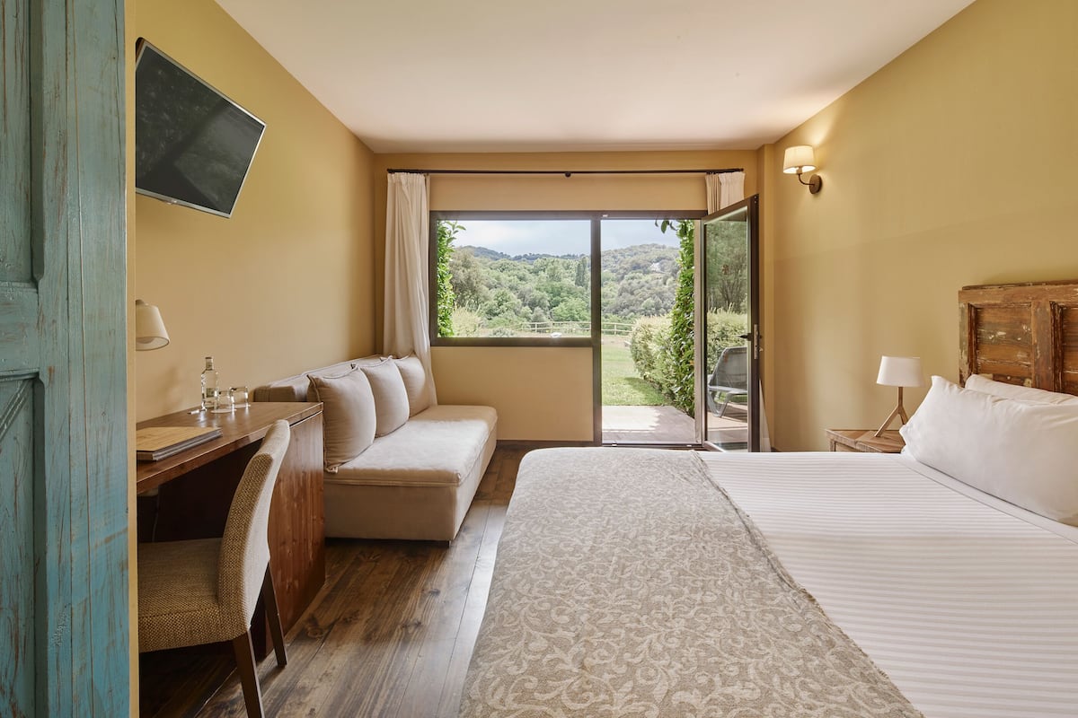 A hotel room with a bed, a desk, a chair, a sofa, and a view of the outdoors.