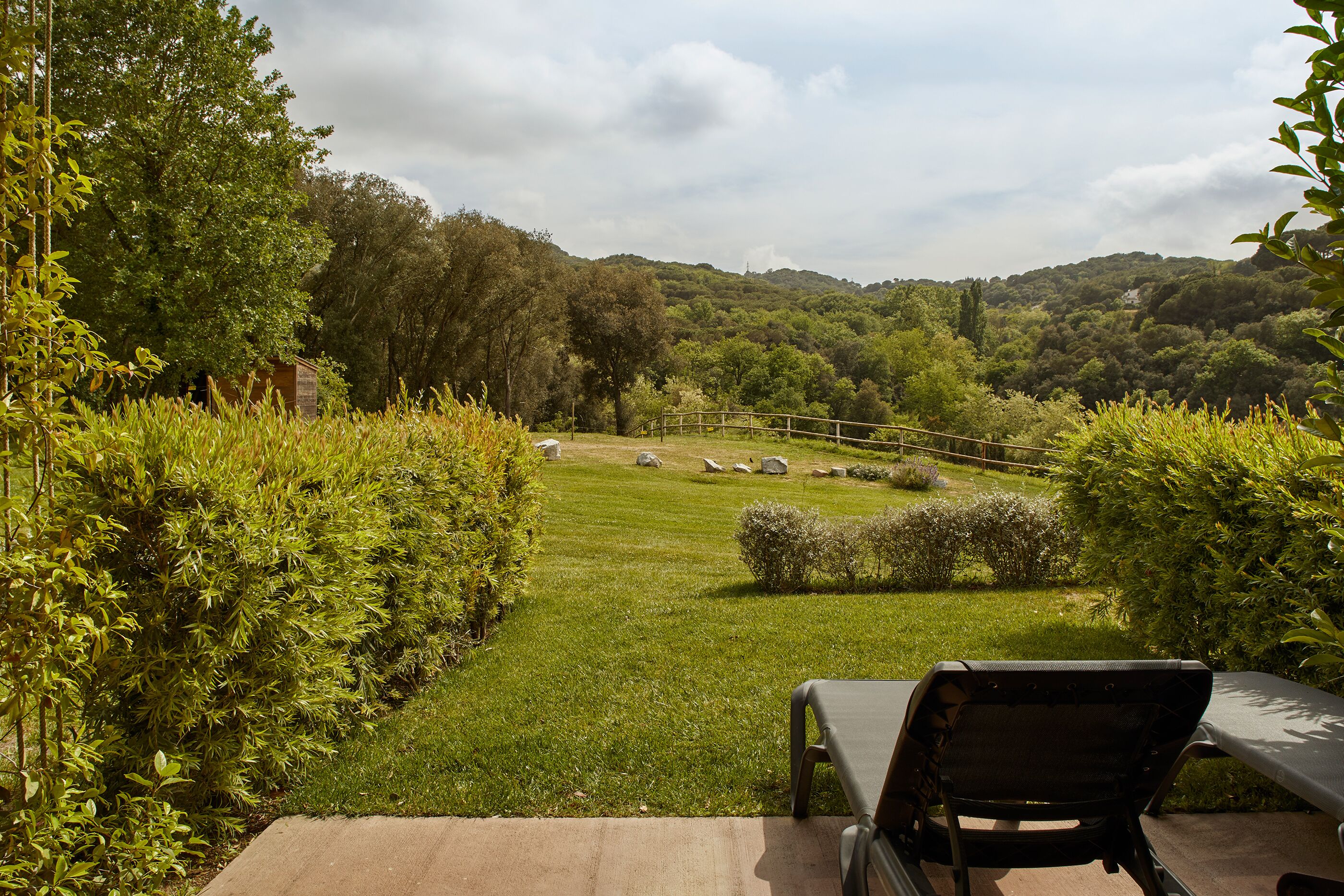 A patio with a chair and a table, overlooking a grassy area with a fence and trees.