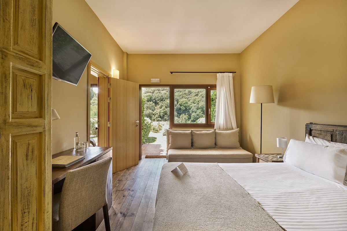 A bedroom with a bed, a desk, a chair, a TV, and a window with curtains.