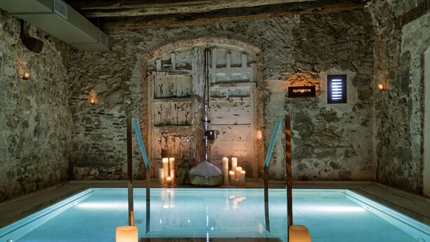 A stone-walled room with a large arched door labeled "FLOTRIUM," a pool with candles, and a sign indicating the room's name. - Mas Salagros Ecoresort & Aire Ancient Baths (Vallromanes)