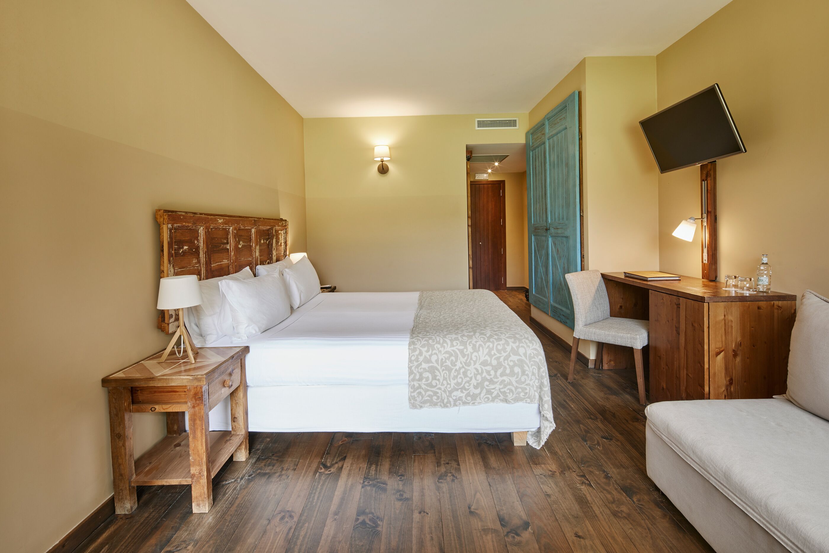 A hotel room with a large bed, a desk, a chair, and a TV mounted on the wall.