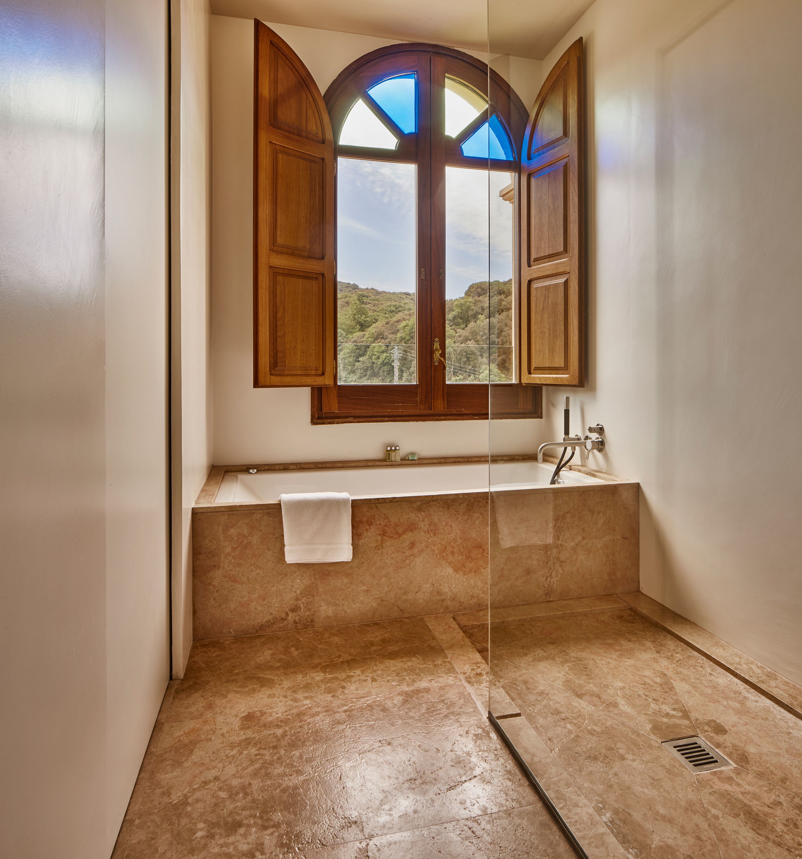Un baño con bañera, una ventana con persianas de madera y una toalla colgada en la pared.
