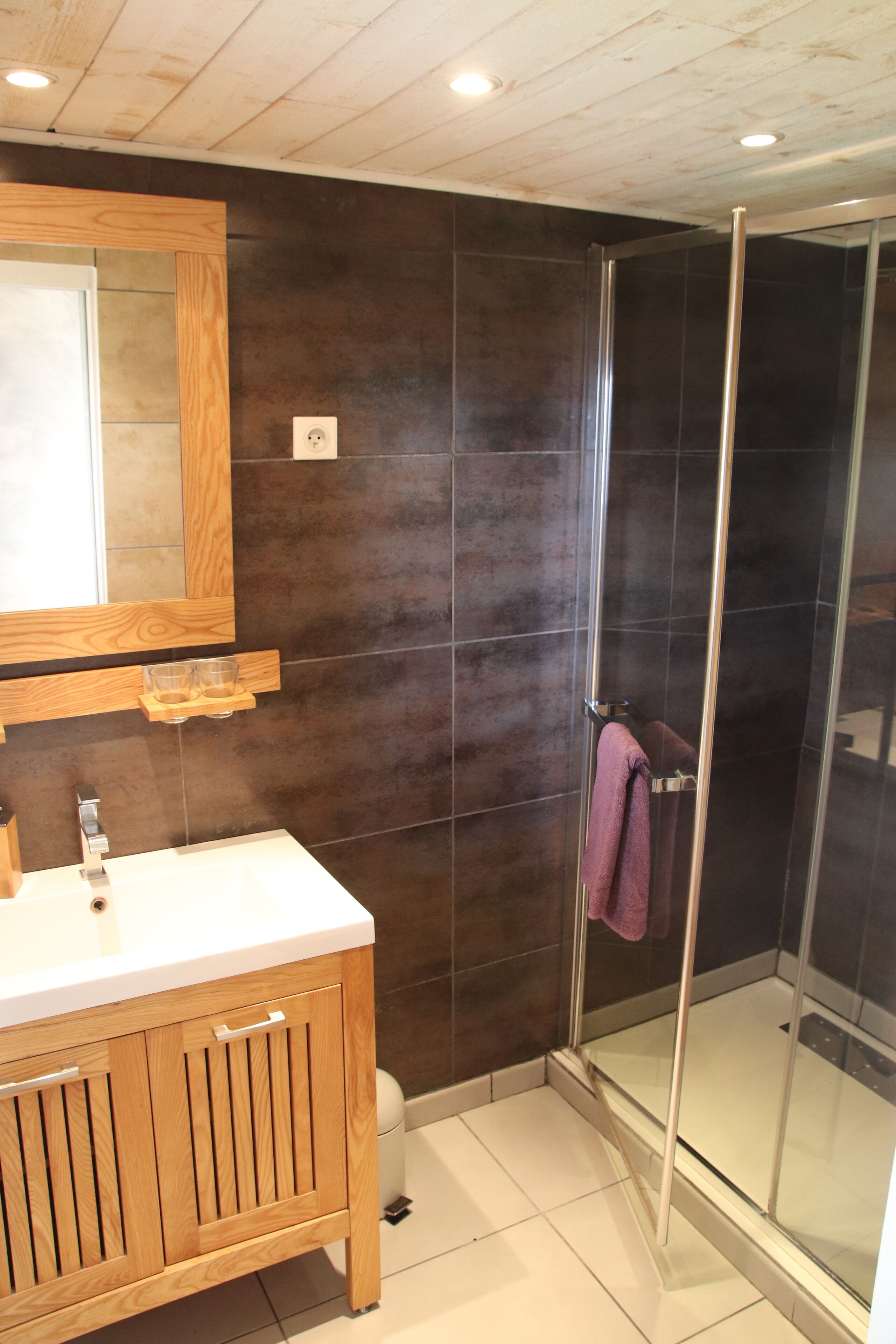 Un bagno con un mobile vanitario in legno, una cabina doccia in vetro e uno specchio sopra il lavandino.