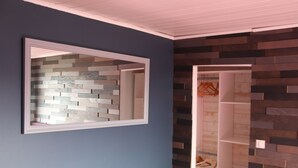 A room with a blue wall, a mirror with a wooden frame, and a shelving unit with a wooden finish.