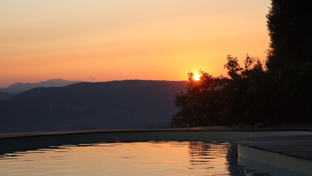 A swimming pool with a sunset view, surrounded by hills and trees.