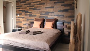 A bedroom with a wooden wall, a bed with two pillows, a nightstand, and a lamp.