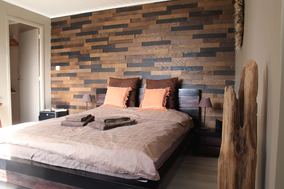 A bedroom with a wooden wall, a bed with two pillows, a nightstand, and a lamp.