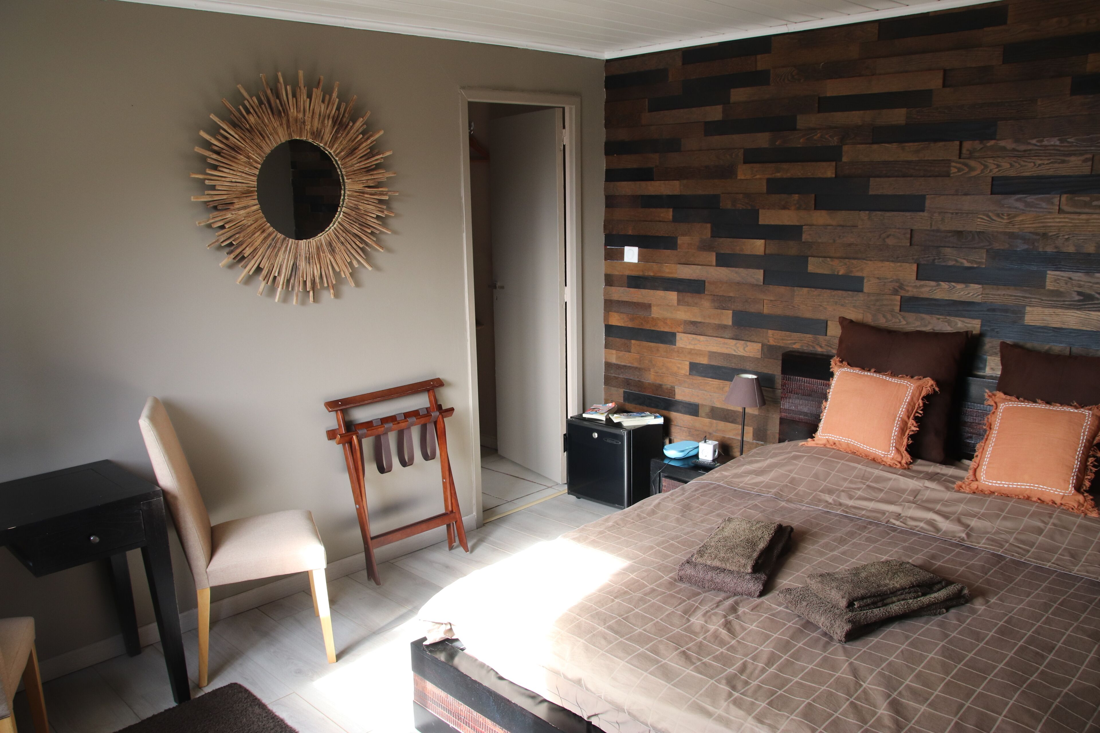 A bedroom with a bed, a desk, a chair, a mirror, and a wooden wall.