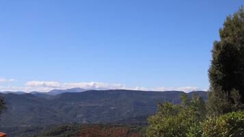 A clear blue sky, a swimming pool with a wooden deck, and a mountainous landscape in the background.