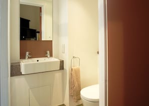 A bathroom with a white sink, two faucets, a mirror above the sink, a towel hanging on a rack, and a toilet.