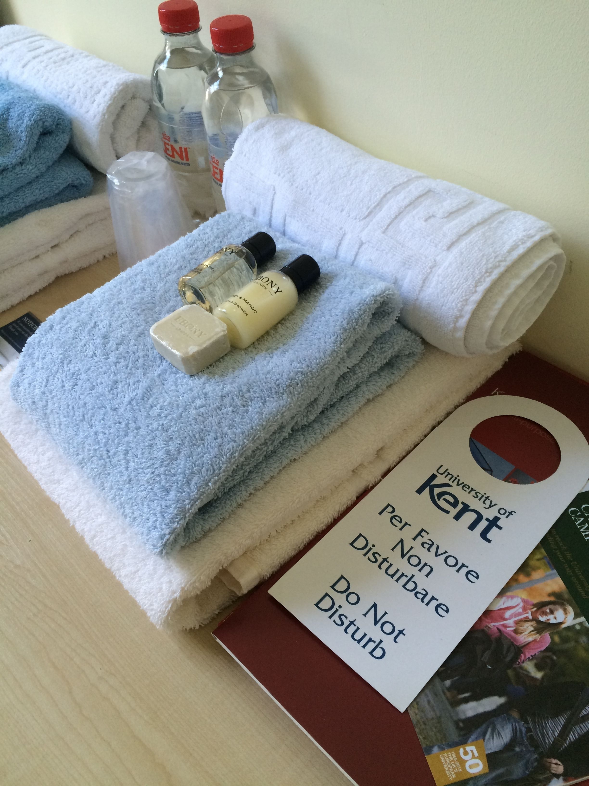 A neatly arranged bathroom with a folded white towel, a blue towel, and toiletries including a bottle of shampoo and conditioner.