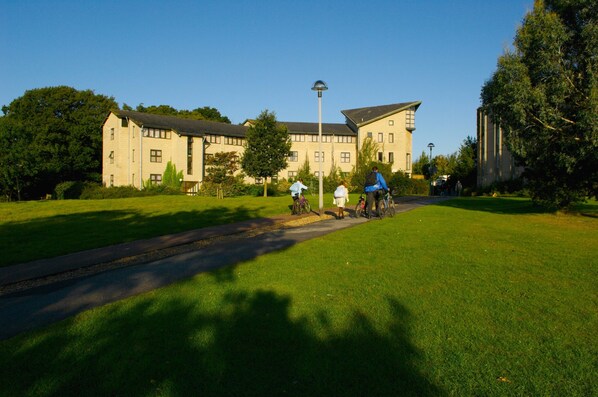 A building with a paved pathway and grassy areas, surrounded by trees and greenery.