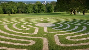 A circular labyrinth garden with a central paved area, surrounded by a grassy field and trees. - Becket Court - University of Kent - Campus Accommodation (Canterbury)