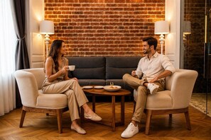 Two people seated on armchairs facing each other with a coffee table between them, a brick wall in the background, and lamps on either side. - Hotel Miniature (Istanbul)
