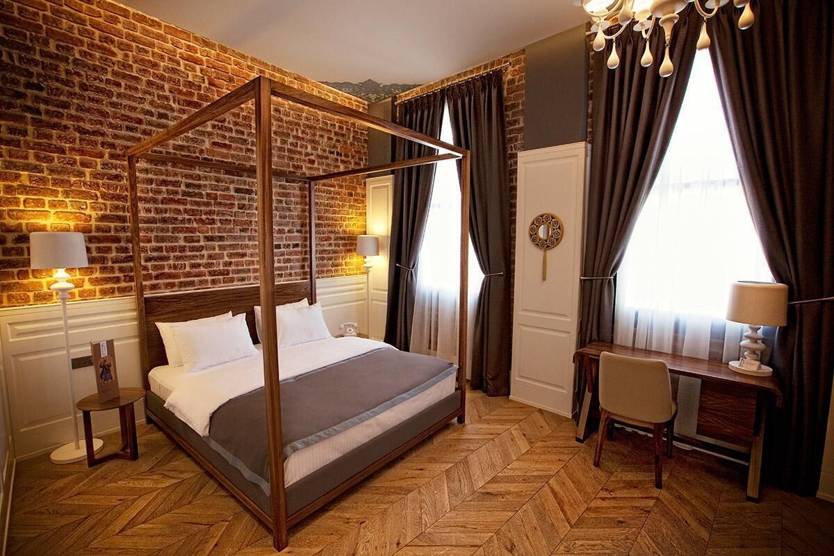 A four-poster bed with a wooden frame, a desk with a chair, and a large window with curtains.