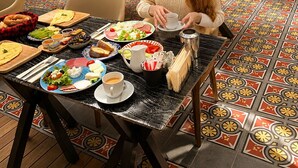 En matplats med ett bord dukat för en måltid, en person som sitter vid bordet och en bänk i bakgrunden.