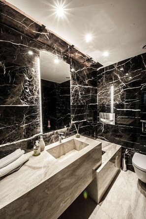 Un baño moderno con un espejo grande, un lavamanos de mármol y un inodoro.
