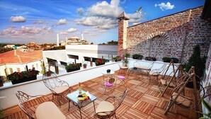 A rooftop terrace with wooden flooring, wicker chairs, a table with fruit, and potted plants. - Hotel Miniature (Istanbul)