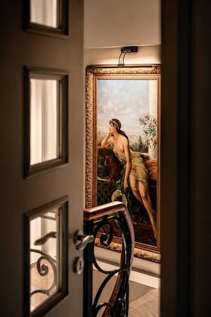 A room with a large ornate mirror reflecting a classical painting, a door with a decorative handle, and a glimpse of a staircase. - Hotel Miniature (Istanbul)