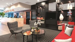 A modern hotel lobby with a reception desk, seating area, and a display of decorative items. - Adina Apartment Hotel Sydney Airport (Mascot)