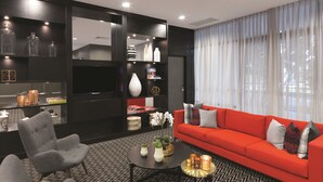 A modern living room with a red sofa, grey armchairs, a black coffee table, and a black and white patterned rug. - Adina Apartment Hotel Sydney Airport (Mascot)