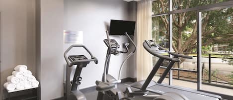 Un gimnasio con máquinas de cardio, un televisor de pantalla plana y un ventanal con vistas a árboles.
