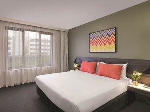 A hotel room with a large bed, a nightstand, a lamp, a window with sheer curtains, and a colorful abstract painting on the wall. - Adina Apartment Hotel Sydney Airport (Mascot)