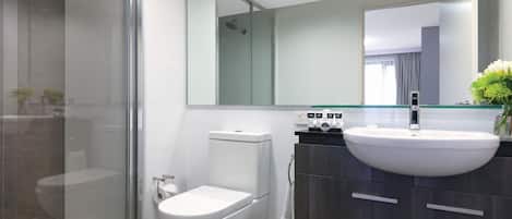 A modern bathroom with a glass shower enclosure, a white toilet, a vanity with a large sink, and a mirror above the sink.
