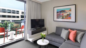 A modern living room with a flat-screen TV, grey sofa, red chairs, and a balcony with a view of buildings and trees. - Adina Apartment Hotel Sydney Airport (Mascot)
