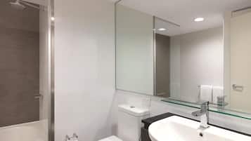 Ein modernes Badezimmer mit einer Glaskabine zur Dusche, einer weißen Toilette und einem großzügigen Waschbecken mit Ablagefläche darüber.